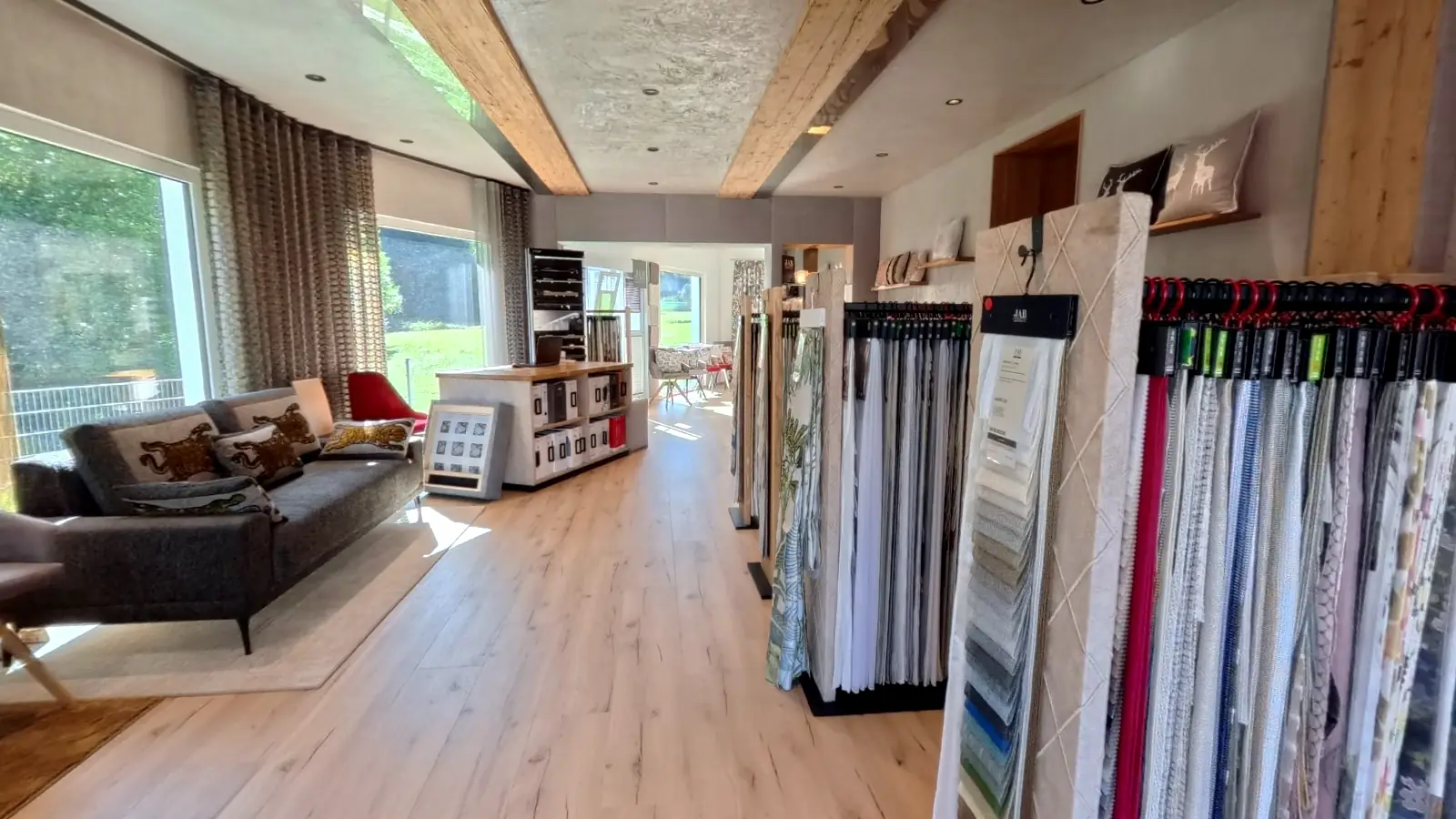 Blick durch den Showroom in Happurg: Sofa am Fenster, lange Reihen mit Stoff- und Gardinenmustern, Holzboden